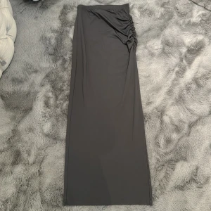Långkjol - Det är en långkjol med tunt material, slits på sidan och längre upp detalj (scrunch) Färg: Mörkgrå Stl XXS men passar även XS /osäker på S. Super fin