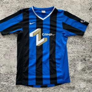 Nike blå och svart fotbollströja, storlek XL, 158-170cm - En blå och svart randig fotbollströja med en guld Z-logotyp på bröstet och texten ”IBRAHIMOVIC 8” på baksidan. Tröjan har en V-ringning och är tillverkad av ett lätt och andningsbart material.  Skick: Mycket bra