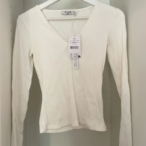 Vit tröja - Vit långärmad tröja i ribbat material. Har en v-ringning vid halsen. Är från NA-KD och är oanvänd med lappen kvar. 