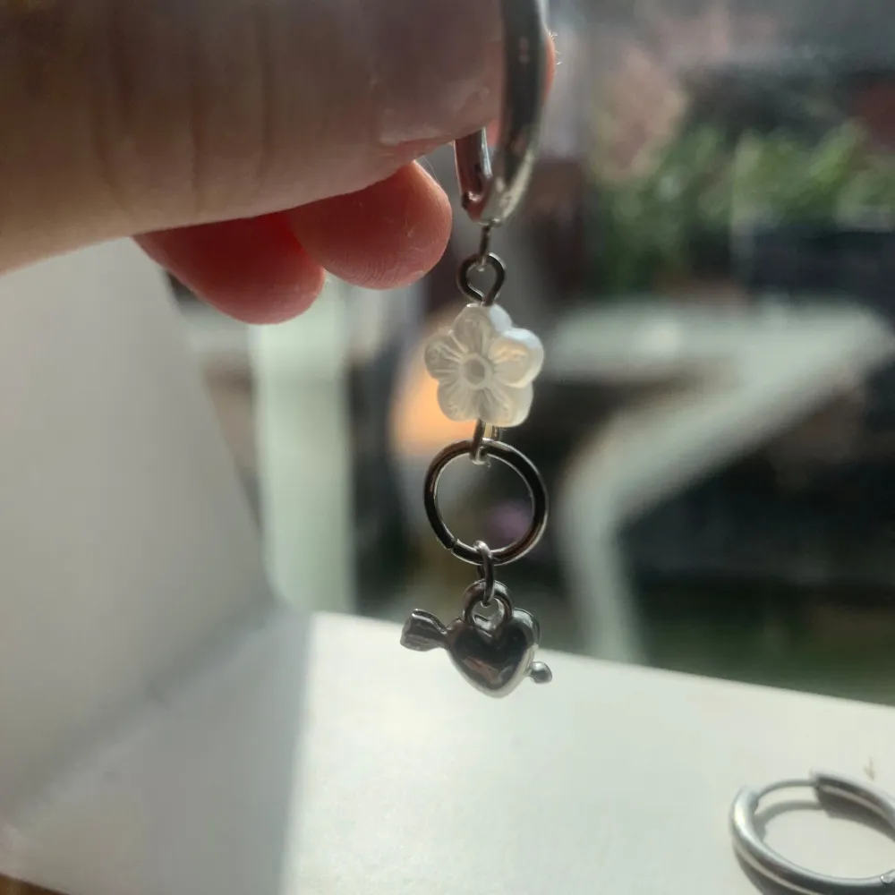 Ett par silverörhänge, varje örhänge har en vit blomma och ett silverfärgat hjärta med en pil genom det. pris går att diskutera vid snabb affär💕. Accessoarer.