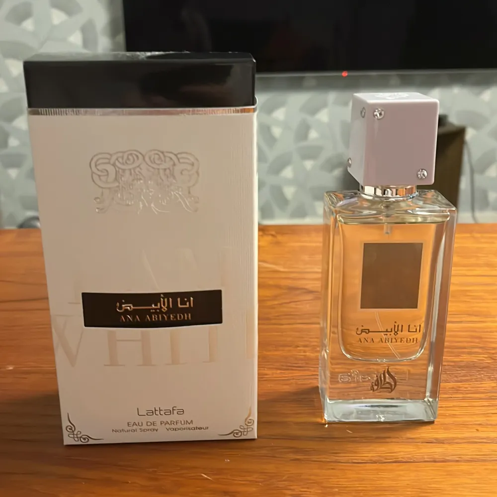 Ana Abiyedh Eau De Parfum från Lattafa är en elegant parfym med en sofistikerad doft. Flaskan är genomskinlig med en vit fyrkantig kork och en guldplatta på framsidan. Förpackningen är vit med guld- och svartdetaljer. Parfymen innehåller noter av trä, mysk och vanilj.. Övrigt.