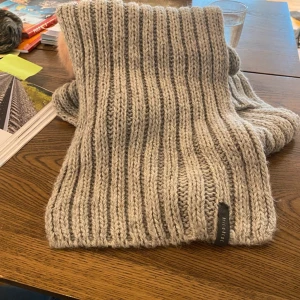 Stickad halsduk -  Mysig, stickad halsduk, ca 200 x 20 cm. Har några trådsläpp, se bilder, men inget som märks när man bär den tycker jag. Fin kvalitet!