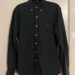 Ralph Lauren skjorta - Säljer den här feta Raffe skjortan i storlek S men passar vissa M. Modell: Slim fit. Färg: Svart med röd logga. Skick 9/10. Vid minsta fundering eller fråga är det bara att skriva🤗