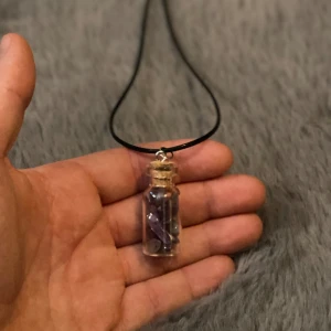 Ametistchips i glasflaska Halsband Handgjort - OBS: Färgvariationer på ametistchipsen och flaskan kan förekomma på grund av de naturliga egenskaperna hos stenen.  Mått längd ca 50cm Glasflaskan ca 3,5cm lång & 1,5cm i diameter.
