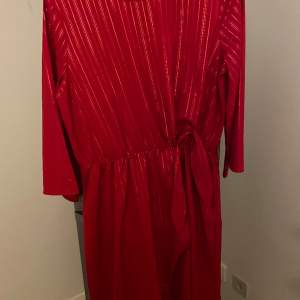 Röd klänning med resår i midjan för skurningen. Omlott klänning med en dekorknut på sidan.  Från Lindex i storlek 170