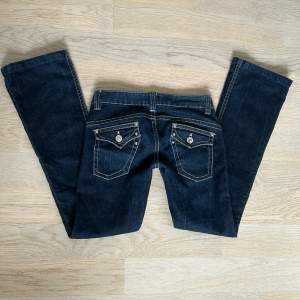 Mörkblåa/svarta jeans med vita sömmar. Snygga bakfickor! Innebenslängd: 77cm. Midjemått tvärs över: 38 cm. Byxorna är uppsydda någon cm. De är lite slitna vid hälarna men det märks inte vid användning.