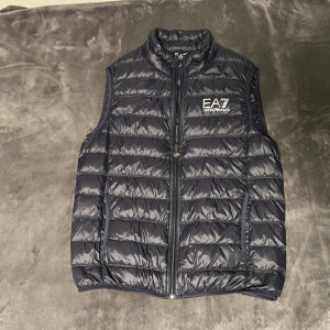 EA7 Emporio Armani väst - Säljer en nästan oanvänd Emporio Armani jacka i storlek L, dock passar den bättre för någon som normalt har storlek M då den är lite mindre i storleken. Västen är i perfekt skick 10/10 med minimal användning.   Nypris 2000kr. 