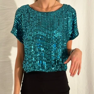 glittrig t-shirt - Glittrig t-shirt i blågrön/teal. Paljetter på framsidan och ett mjukt stretchigt tyg i ryggen. I och med det stretchiga tyget så passar den XS-L beroende på vilken passform man är ute efter. Tjejen på bilden har i vanliga fall XS-S