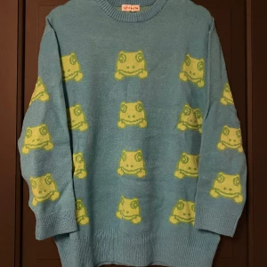 Stickad tröja med grodor  - En blå stickad tröja med grodor som mönster. Den är storlek XS men oversize, så den skulle passa en med storlek S också. Helt oanvänd med lappen kvar! 🌷