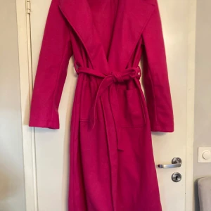 Kappa strl L (40/42)  - Cerise rosa kappa i strl 40/42 (L). Kappan har skärp i midjan och fickor på sidan.  Kappan är helt ny, aldrig använd.  Köpt från Shein. Material: 100% polyester  Fler bilder kan skickas. 