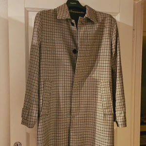 Biege lång kappa - En lång biege rutig kappa. Sälj pågrund av att den aldig används