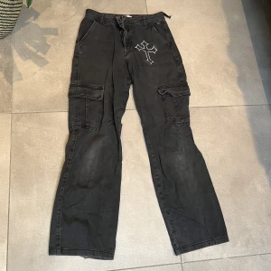 baggy cargopants med tryck - Baggy cargojeans med självmålat kors vilket gör dom helt unika! Man ser på bilden att en sån som håller bältet är av men det går enkelt att sy fast igen! Jag säljer för att jag TYVÄRR har växt ut dom:(