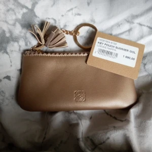 Key pouch summer gold  - Säljer en helt oanvänd liten väska från Loewe köpt på NK används för nycklar men kan såklart ha annat smått i också. Nypris 1690 kr säljer den för 1200 kr