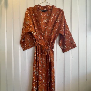 Sissel Edelbo Kimono Magnolia - Knälång Kimono med 3/4 ärmar från Sissel Edelbo. Kimonon har ett avtagbart bälte i samma tyg som Kimonon. Sissel Edelbos plagg är alltid unika och skapade genom att återanvända Saris från Indien, från en kvinna till en annan. Kimonon är helt oanvänd.
