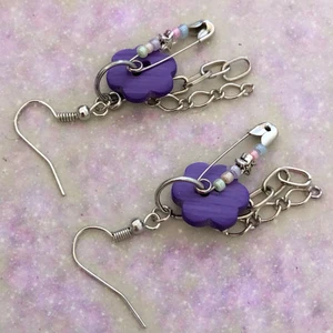 Örhängen - Örhängen!! Har lila knappar och säkerhetsnålar med pärlor i pastellfärger. Två olika kedjor hänger bakom knappen🌸💜 De är 4 cm på längden och 1,5 cm på bredden. Säljer för 50kr + 12kr i frakt!