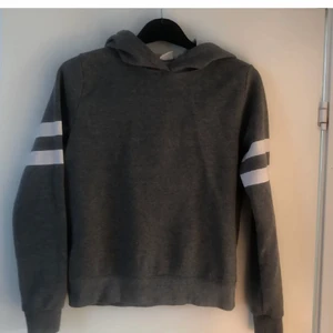 Grå hoodie stl S Gina tricot - Mörkgrå hoodie stl S Gina Tricot. Vita printade ränder i ärmarna. Bra skick. Bomullsmaterial inuti.