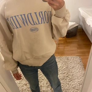 Beige hoddie  - En jättefin och mysig beige hoddie med blå text på. Hoddien är inte använd många gånger men den har dock en liten fläck på sig som man knappt ser.
