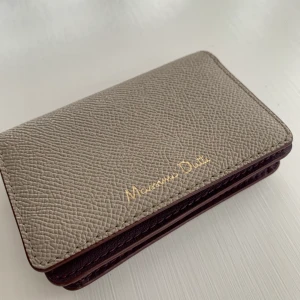 Plånbok från Massimo Dutti - Beige/grå plånbok med vinröd insida från Massimo Dutti. Myntfack med dragkedja på baksidan. Helt felfri, som ny! Storlek 11 cm x 7,5 cm. Läderimitation. 