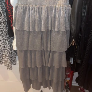 Volangkjol - Silvrig lång kjol från NA-KD. Köpte den för 3 år sedan men har aldrig använt den på grund av att den förut inte passade och nu har jag väldigt många liknande. Passar PERFEKT till nyår😍 Den är rätt lång, nedanför knäna på mig som är 168 cm. I midjan skulle jag säga att den passar allt från XS-M