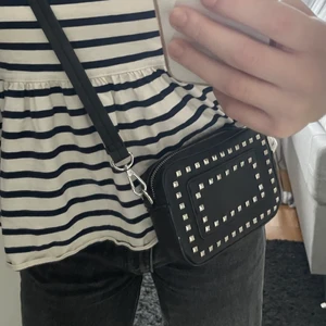 Axelremsväska  - Säljer denna coola väska med nitar och snygg form. Justerbart band och innerfack. Ca 18x13cm. Köpare står för frakten!💗