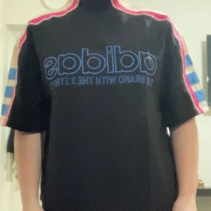 Adidas T-shirt  - Jag säljer denna Adidas T-shirt. Ett fint original från Adidas. Jag säljer eftersom att de inte riktigt är min smak. T-shirten ska påminna om rebelliskt 90-tal. Det är en helt oanvänd tröja och är då i väldigt bra skick. Materialet är inte stretchigt och ganska hårt och det står att den är tillverkad av lätt crepematerial. Den har en liten fläck på högra baksida axeln, vet inte varför men de är inget man tanker på och det går förmodligen att tvätta bort.