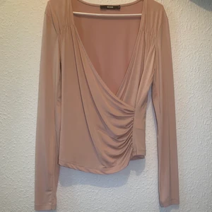 Krås slätt ljus rosa blus strl M - Oanvänd blus från bikbok i storlek M, kramar om kroppen. Färgen är ljus rosa men lutar sig även åt det beiga hållet. Materialet är nylon och ger åven en glans.