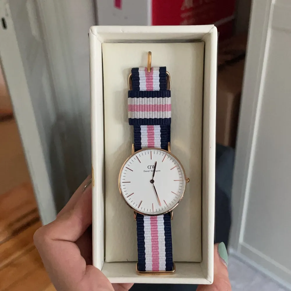 Säljer min oanvända Daniel Wellingtonklocka med uret i roseguld och bandet i tyg av färgerna vitt, rosa och marinblått.. Accessoarer.