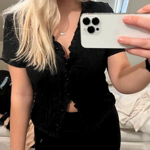 T-shirt - Svart stickad t-shirt med volanger och knappa, kan användas öppen också som en liten kofta