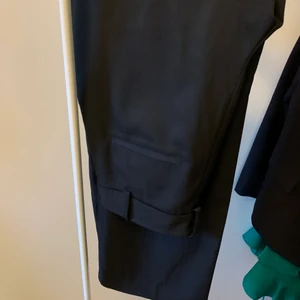 Svarta kostymbyxor Gina Tricot stlk 36 - Svarta kostymbyxor från Gina Tricot i något glansigare tyg. Storlek: 36.  Pris: 100 + 66kr. 97% polyester 3% elastan. Fint skick, inget att anmärka på! Byxorna är inte speciellt tighta utan sitter mer löst runt om benen med ett fint rakt fall. Innerbensmåttet är 76cm från kryssömmen i grenen ner till byxbenets kant. 