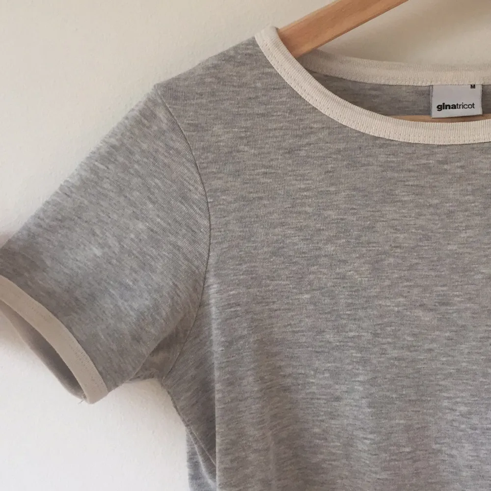 En grå t-shirt med vit linjering längs ärmarna och kragen. Strl M men sitter som en S/M. T-shirts.