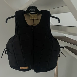 Svart ridväst Racesafe XS - En svart ridväst som är använd ett förtal gånger. Otroligt skön, sitter snyggt och Racesafe säkerhetsväst är CE-märkt, testad samt godkänd enligt senaste kraven EN1384 & EN 13158 och BETA 2009 level 3, vilket motsvarar de hårdaste kraven på säkerhetsvästar för ridning. Inte alls smutsig utanpå, finns lite dammfläckar inuti men inget som färgar eller märks av. Bara använt ett fåtal gånger pågrund av att jag slutade på ridning ganska tätt inpå. Köpt för 2798kr. Passar mig perfekt