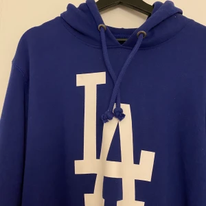 BLÅ HOODIE - Blå hoodie med LA-tryck. Aldrig använd. Köpt på Stadium. Storlek L.