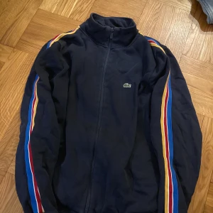Lacoste zip up - Lacoste zip up/sweater. Barnstrl 176 men passar mig som är en 36a. Mkt fint skick, tyvärr gör bilderna inte tröjan rättvis då den är djupblå/marinblå och inte svart. 