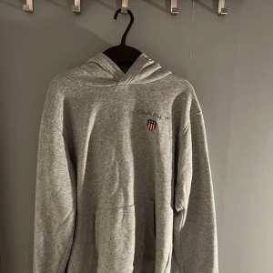 Gant huvtröja Shield logo, (grå) - Visar mindre tecken på användning, är något nopprig (går att fixa för den som har lite tid) men är i övrigt felfri.