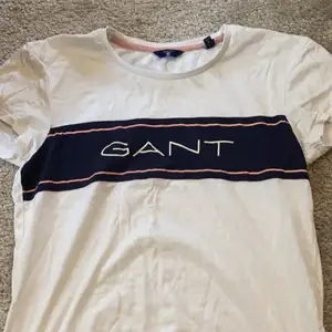En Gant tröja som är vit med mörkblåa och rosa detaljer.Det finns en lite fläck på tröjan men det är inget som syns så mycket.