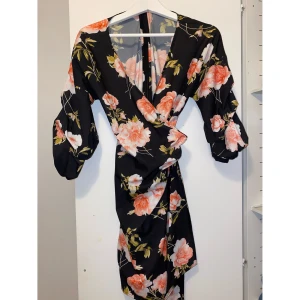 Blommig klänning Nelly  - Blommig omlottklänning från Nelly. Den har även lite puffarmar och band runt midjan. Har använts endast 1 gång. Den är som helt ny. 