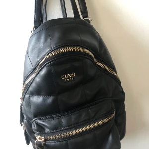 Ryggsäck från Guess - Säljer denna snygga ryggsäck från Guess då jag tyvärr inte fått så mycket användning av den. Har endast använt den ett fåtal gånger alltså är den fortfarande i mycket gott skick. Börja buda från 200 i kommentarerna eller köp direkt för 550kr. Frakt ingår ej. 