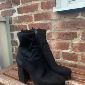 Svarta klackar med högt skaft  - Svarta klackskor med högt skaft, perfekt att bära till klänning eller jeans. Skorna har en dragkedja på insidan av skon. Materialet är av mocka imitation. Använda 2 gånger så i fint skick.