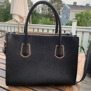 Svart väska från hm - Söt svart väska från hm med gulddetaljer. Den är 35x27 cm. Väskan är ganska använd så det finns slitage på den. Säljer den pga att jag sällan använder den. 66kr i frakt💕💕