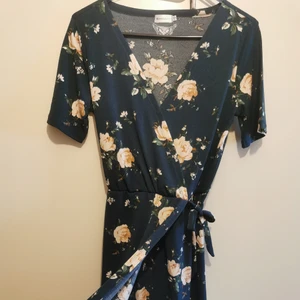 Omlottklänning - Fin blommig omlottklänning från Lager157. Resår i midjan och fejk-knytband (fastsytt i sidor), även omlott delen är ihopsydd framtill. Mörk blå/grön(aktig) färg. Aldrig använd, men lappen är tyvärr borttagen. (Lägger all frakt på spårbart, men går ev att få billigare med porto)