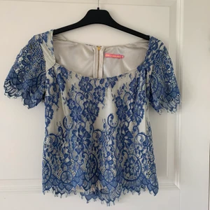 Top - Säljer en tröja från Pernilla Wahlgrens collection, vit och blå i spets mer gullig dragkedja baktill. Storlek S, säljer för 200kr. Frakt tillkommer!