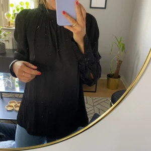 Sidenblus med hög krage från H&M - Sidenblus med hög krage från H&M. Svart med gråa prickar. Sparsamt använd. Storlek 42.