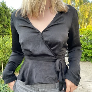 Svart satinblus - Supersnygg svart satinblus med omlottknytning i midjan från NLY Trend. Skjortknappar på ärmarna och säkerhetsknäppning vid bysten. Storlek S men passar XS/M då man bestämmer knytningen själv. Använd 1 gång. Säljs för att den inte kommer till använding. Frakt tillkommer 💜