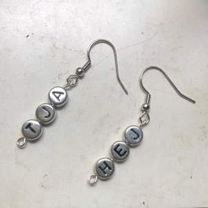 Ett par handgjorda örhängen som är silverfärgad med texten ”HEJ” och ”TJA”