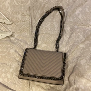 Axelväska från FLORA&CO - En ca 25 cm bred axelväska med svart kedja, använd några fåtal gånger men nästan i nyskick. Det finns två fak med kedja, ett på baksidan och ett inuti, men även två fak utan dragkedja på insidan. Väskan går att stänga med både dragkedja och magnetisk knapp. :) priset är exklusive frakt