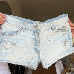 Ljusblå jeansshorts med pärlor - Snygga ljusblå jeansshorts från Gina Tricot med slitna detaljer och små pärlor över hela framsidan. Säljer dom då de är för små för mig, jättebra skick och helt felfri! Finns inte kvar på hemsidan längre. Pris kan diskuteras.💕