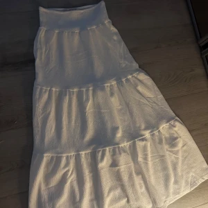 Vit långkjol från 157 med volanger - Supersöt vit långkjol från 157 med bred smock i midjan och flera volanglager. Kjolen är lätt och flowy, perfekt för varma dagar. Enkel att styla med crop top eller hoodie för en chill vibe. Endast provat på då den är för lång för mig som är 157cm! Skicket är helt ny köptes för 3 v sedan.