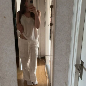 Vita linnebyxor från Alobha  - Säljer ett par vita linnebyxor med avslappnad passform och snörning i midjan. Byxorna är raka i modellen och har en luftig känsla, perfekta för varma dagar. De är tillverkade i linne och har en enkel, stilren look. De är uppsydda så de ska passa mig som är typ 163cm. Aldrig kommit till användning!