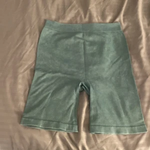 Gröna ribbade shorts från H&M - Snygga gröna ribbade shorts från H&M i midwaist-modell. De är stretchiga och sitter skönt, perfekta för sommaren eller träning. Materialet är en blandning av bomull och polyamid som ger en mjuk känsla och bra passform.