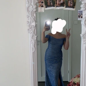 Glittrig blå långklänning offshoulder - Säljer en glittrig blå långklänning med offshoulder och slits framtill. Klänningen är i storlek 38 men kan funka på en 40. Den är ändats använd en kväll och är i ett väldigt bra skick. Pris kan diskuteras vid snabbköp.